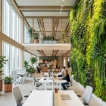 Moderne kantoorruimte met levende plantenwand, witte bureaus en grote ramen die natuurlijk licht binnenlaten