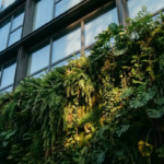 Weelderige verticale groene gevel met tropische planten en dicht gebladerte op modern gebouw, zonlicht filtert door de bladeren.