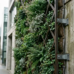 Verticaal groen wandsysteem op modern gebouw met klimplanten door geometrisch metalen trellis, zichtbare beugels in beton.