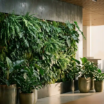 Verticale groene plantenwand met mos- en saliegroen gebladerte in modern kantoorinterieur, keramieken plantenbakken aan de basis.