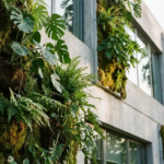 Verticale groene plantenwand met Monstera-bladeren, varens en mos op een modern kantoorgebouw van beton.