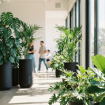 Weelderige tropische planten waaronder Monstera deliciosa en Kentia palmen in moderne kantoorruimte met betonvloer en grote ramen