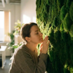 Persoon ruikt aan weelderige groene moswand in modern kantoorinterieur met natuurlijk licht