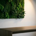 Bewaarde moskunst aan witte muur met smaragdgroene texturen, verlicht door spotlight boven modern bureau.