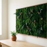 Ingelijst mospaneel met smaragdgroene texturen aan een warme witte muur, met een modern bureau en terracotta plantenpot op de voorgrond.