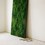 Vers geïnstalleerd mosspaneel met smaragdgroene texturen tegen witte muur, omringd door installatiegereedschap op betonnen vloer.
